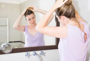 Femme s'attachant les cheveux en se regardant dans le miroir de la salle de bain